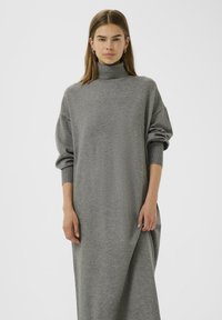 Šedé oversized rolákové šaty vyrobené z měkkého úpletu, s dlouhými rukávy a volným střihem, dosahující po kotníky.