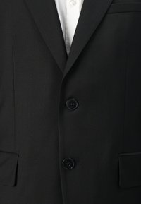 Black suit jacket featuring a notched collar, two front pockets, and two button closures. Material has a smooth, textured finish.