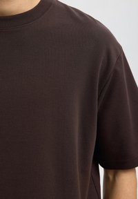Brun bomull t-skjorte med rund hals, korte ermer og en jevn tekstur, med en løs passform og uten synlige mønstre eller grafikk.