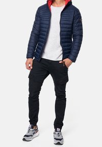 Navy puffer jacket with a red hood, ribbed cuffs, and zipper. Paired with black cargo pants and gray sneakers with accents.