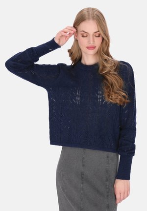 Pull court bleu marine en tissu tricoté avec un motif texturé. Manches longues avec poignets côtelés. Assorti à une jupe grise.