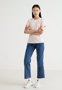 T-shirt ajustada rosa claro com mangas curtas, combinada com jeans de perna reta azuis e sapatilhas brancas. Design simples e limpo com um estilo casual.