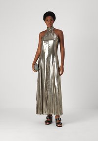 Metalna srebrna halter maxi haljina ima elegantnu kroj, leteći materijal i glatku teksturu, u kombinaciji s malom zelenom torbicom i crnim cipelama.