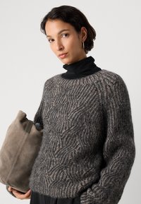 Teksturowany szary, oversize sweter z falistym wzorem, noszony na czarnym golfie. Dodatki to miękka szara torebka.