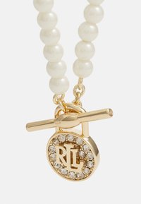 Collier en perles blanches avec un fermoir en or et un pendentif rond orné de cristaux transparents et des initiales "RL".