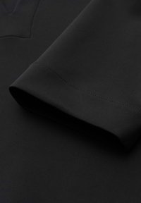 Gros plan sur le poignet et la couture cousue d’une chemise noire à manches longues sur une surface de tissu lisse.