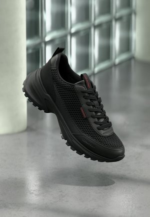 Sneaker nero Calvin Klein con tomaia in mesh, collo imbottito e suola robusta, mostrato sospeso sopra un pavimento in cemento.