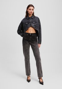 Chaqueta de mezclilla negra recortada con bolsillos frontales y cierre de botones, combinada con jeans negros de cintura alta, ambos con una textura deslavada.