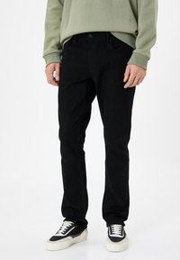 Vaqueros de mezclilla negros con corte recto, textura sutil, cinco bolsillos y cierre de botón, combinados con un sudadera verde clara y zapatillas deportivas.
