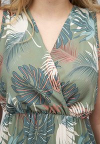 Green dress with a wrap design featuring a palm leaf print in blue, pink, and white. Textured fabric, flattering waist elastic.