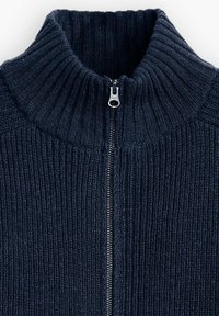 Suéter de punto azul marino con un cuello alto y cremallera plateada de longitud completa. Presenta una textura acanalada y líneas verticales a lo largo de la tela.