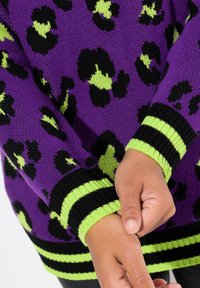 Maglione lavorato a maglia viola con un motivo leopardato nero e verde. Polsini a coste con strisce nere e verdi. La texture sembra morbida e accogliente.