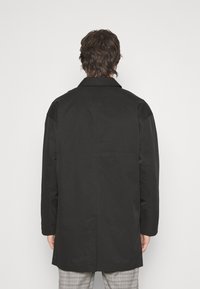 Abrigo negro en un material ligero con un corte recto, cuello en punta y mangas largas, con un diseño minimalista y sin herrajes visibles.