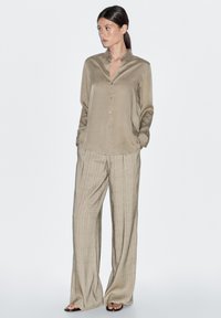 Satin beige overhemd met knopen en lange mouwen, gecombineerd met lichte geruite wijde broekspijpen in beige tinten. Gladde textuur, ontspannen pasvorm.