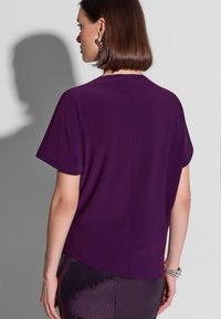 Fioletowa bluzka z krótkim rękawem wykonana z gładkiej tkaniny, o luźnym kroju i prostym dekolcie, zestawiona z błyszczącym, teksturowanym dołem.