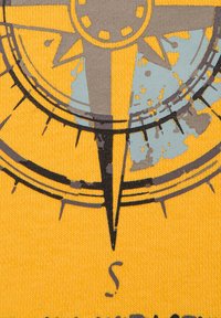 Żółta tkanina z wzorem kompasu w odcieniach szaro-niebieskich, o teksturowanym wyglądzie i postarzanych detalach. Punkty kompasu zaznaczone wyraźnie.