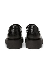 Chaussures en cuir noir avec un bout arrondi, une semelle plate et un logo en relief sur le talon. Le design présente une texture lisse et des accents minimaux.