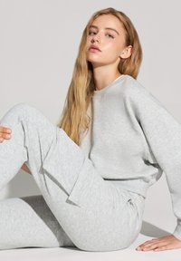 Jasnoszara, miękka bluza z okrągłym dekoltem i długimi rękawami, w zestawie z dopasowanymi spodniami zwężającymi się ku dołowi, z bocznymi kieszeniami.