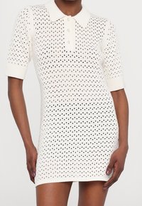 Robe polo en tricot ivoire avec un motif à pois, manches courtes et col à bouton. Texture douce et coupe ajustée.