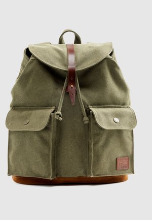 Sac à dos en toile vert olive avec une sangle supérieure en cuir, deux poches avant et une base en cuir marron. Comprend une fermeture à cordon et un patch logo.