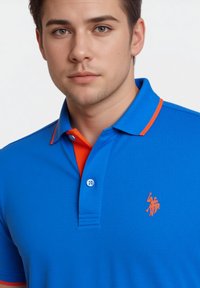 Blå polo-shirt med orange kravekanter og broderi. Har en to-knaps placket og korte ærmer. Glat tekstur og tætsiddende design.