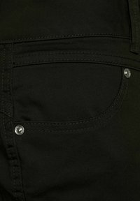 Czarne dżinsy denimowe z tylną kieszenią z kontrastowym przeszyciem i srebrnym detalem w postaci nitów. Tkanina wydaje się gładka z delikatnym połyskiem.