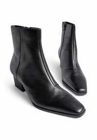 Botines de cuero negro hasta el tobillo con puntera puntiaguda, textura suave, cremalleras laterales y un tacón bajo en bloque. Diseño simple y elegante.