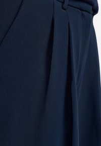 Tessuto blu navy con una texture liscia, caratterizzato da pieghe e dettagli di cucitura sottili, progettato per pantaloni sartoriali.