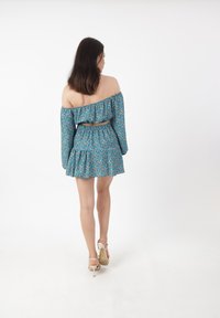 Abito off-the-shoulder a maniche lunghe in teal con motivo floreale; dettagli a balze e vita elastica; gonna svasata; abbinato a tacchi leggeri.