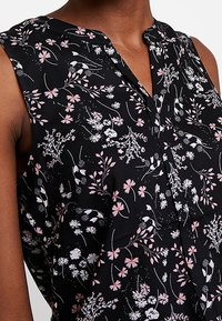 Schwarze ärmellose Bluse mit floralem Muster in Pink und Weiß, mit einem V-Ausschnitt und einer Knopfleiste vorne.