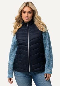 Marinefarbene Steppweste mit vertikalen Nähten, strukturierten blauen Ärmeln und einem frontalen Reißverschluss. Verfügt über elastische Bündchen und ein tailliertes Design.