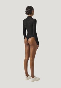 Svart långärmad bodysuit med hög krage, ribbad textur och låg skärning i ryggen, ihopparad med vita sneakers.