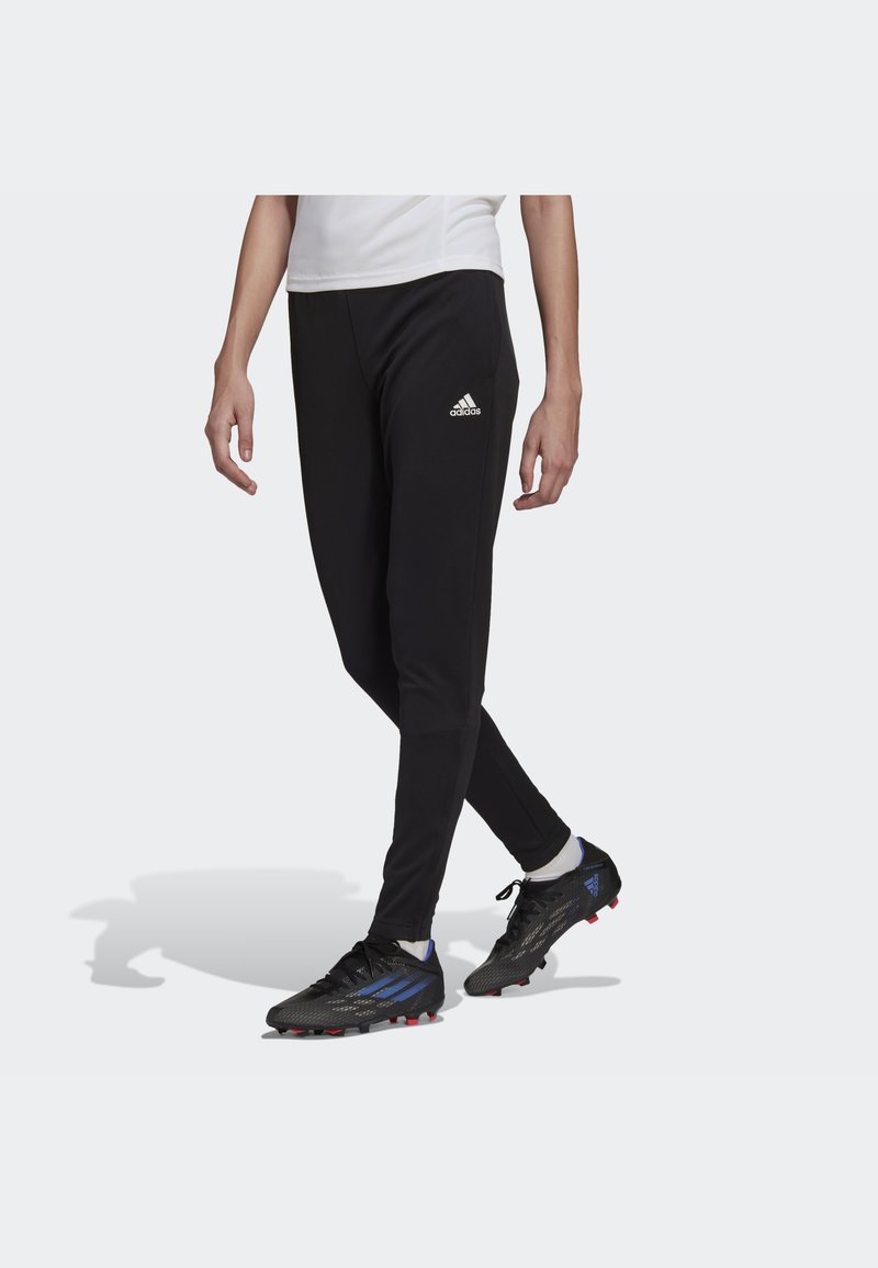 Black athletic pants with fitted design, logo on left thigh, and subtle texture. Paired with black soccer cleats featuring blue accents.