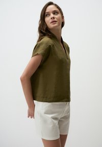 Top in lino verde oliva con scollatura a V e maniche corte, abbinato a pantaloni corti bianchi. Design semplice con vestibilità rilassata e tessuto testurizzato.