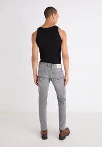 Grå jeans med stickade detaljer, som bärs med en svart linne. Bruna stövlar har en kraftig sula. Visar framhäver bakvyn och passformen.