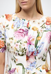 Bloemenjurk met een mix van levendige bloemen in roze, oranje, geel en blauw op een witte achtergrond; korte mouwen en een aangesloten lijfje.