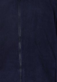 Giacca in pile blu navy con zip a tutta lunghezza, texture liscia e design minimalista. La vista ravvicinata mette in evidenza i dettagli della zip e del tessuto.