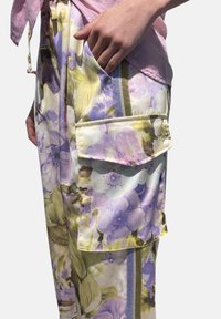 Pantaloni con motivo floreale in colori pastello, dotati di ampie tasche laterali, una texture morbida e strisce metalliche decorative.