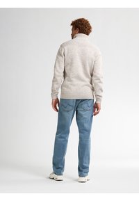 Vaaleanharmaa neulepaita, jossa on korkea kaulus ja teksturoitu olkatyynytys, yhdistettynä sinisiin farkkuihin ja valkoisiin tennareihin.