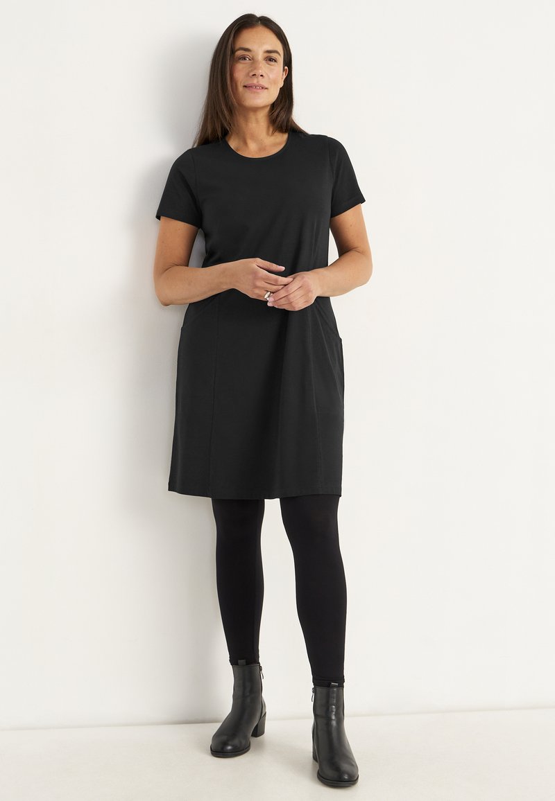 Svart kortärmad klänning med rund halsringning, avslappnad passform, två sidofickor, kombinerad med svarta leggings och ankelstövlar.
