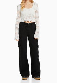 Witte, gestructureerde, gebreide crop sweater met lange mouwen en een open patroon, gecombineerd met losse zwarte cargobroeken met zijzakken.