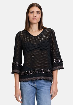 Top in rete nera con scollatura a V e maniche a tre quarti, caratterizzato da un bordo di paillettes e dettagli frangiati all'orlo.