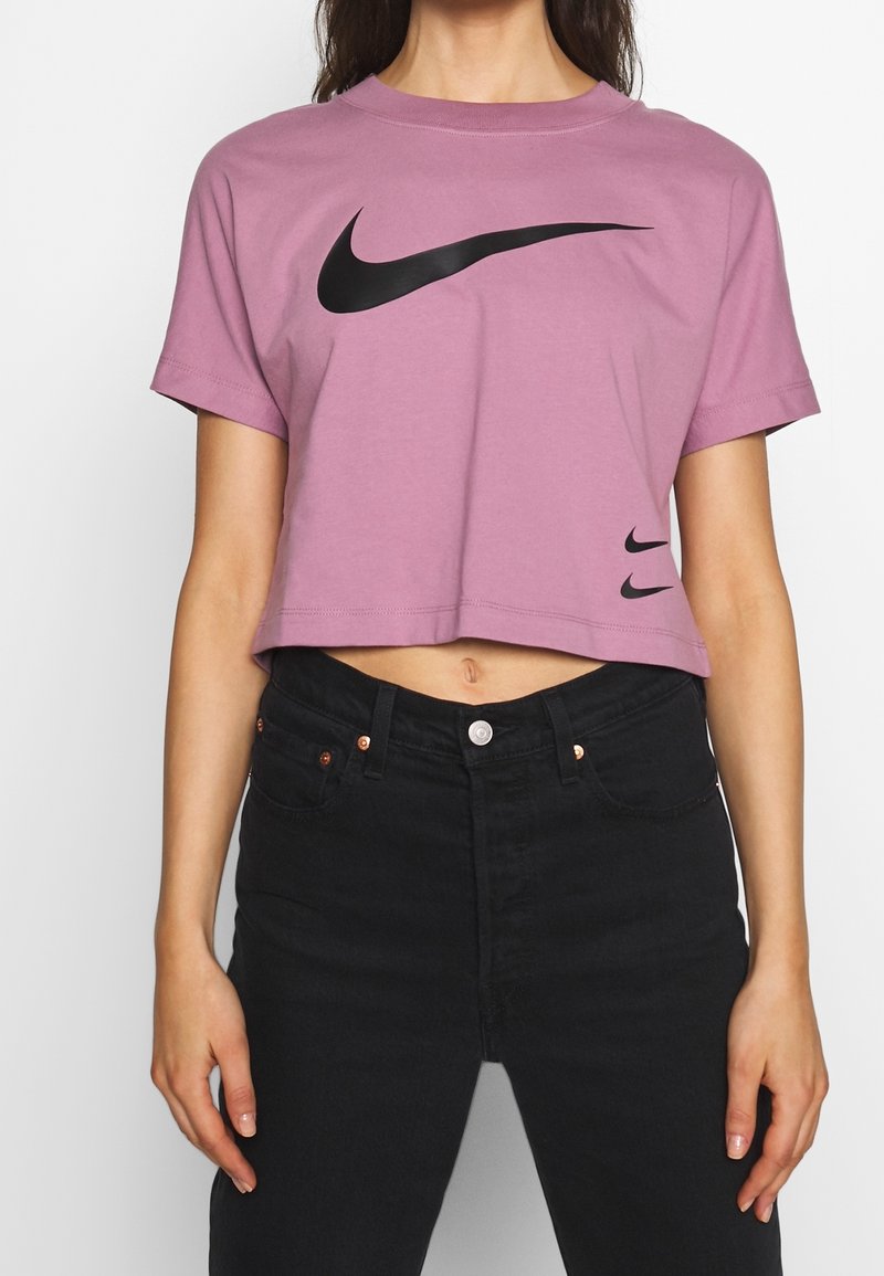 Ljusrosa kortärmad t-shirt i bomull, med en stor svart Nike swoosh-logotyp fram och en mindre logotyp nära fållen.