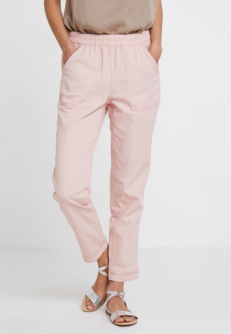 Růžové bavlněné kalhoty s elastickým pasem, se bočními kapsami a volným střihem, ukončené manžetami na kotnících, doplněné o stříbrné sandály.