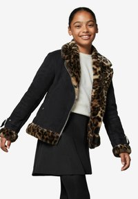 Sort jakke med leopardprint faux fur krave og manchetter, lynlås-lukning, kombineret med en hvid sweater og sort nederdel, bæres af en ung person.