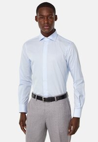 Camisa de vestir a rayas azul claro y blanca con cuello spread y mangas largas, combinada con pantalones grises y un cinturón negro.