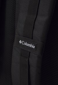 Black backpack strap featuring a woven texture, mesh fabric, and a visible Columbia logo tag. The design includes sturdy stitching and accents.
