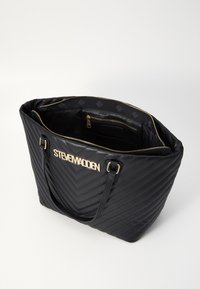 Tote torba crne boje s uzorkom u obliku chevrona i zlatnim logotipom. Ima zatvaranje na patentni zatvarač, dva naramenka i teksturirani sintetički materijal. Obložena unutrašnjost.