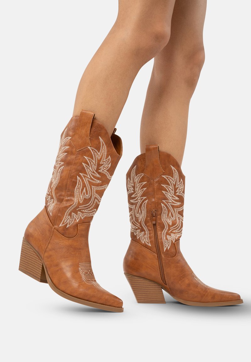 Botas vaqueras de cuero marrón con puntas afiladas, intrincados bordados blancos, tacones de bloque de altura media y una cremallera lateral para una fácil puesta.