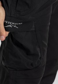 Sorte udendørsbukser med en sidelomme og et mærkat, der viser "WEDEMOUNT." Materialet ser holdbart ud med en glat tekstur.